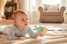Baby liegt auf einer weichen Decke im hellen Wohnzimmer und entdeckt neugierig ein altersgerechtes Holzspielzeug
