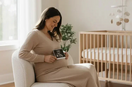 Schwangere Frau sitzt im hellen Babyzimmer und hält liebevoll ein Ultraschallbild vor ihren Babybauch
