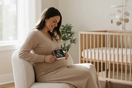 Schwangere Frau sitzt im hellen Babyzimmer und hält liebevoll ein Ultraschallbild vor ihren Babybauch