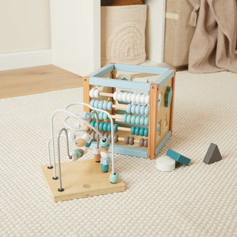 Holz-Motorikwürfel in Pastellfarben mit Zählrahmen, Kugelbahn und Formen-Steckspiel auf hellem Teppich – fördert Motorik und Koordination, erhältlich bei BabyLions.