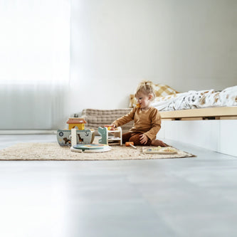 Kleinkind spielt mit Holzspielzeug im hellen Kinderzimmer auf einem Teppich, geeignet für Babys und Kleinkinder