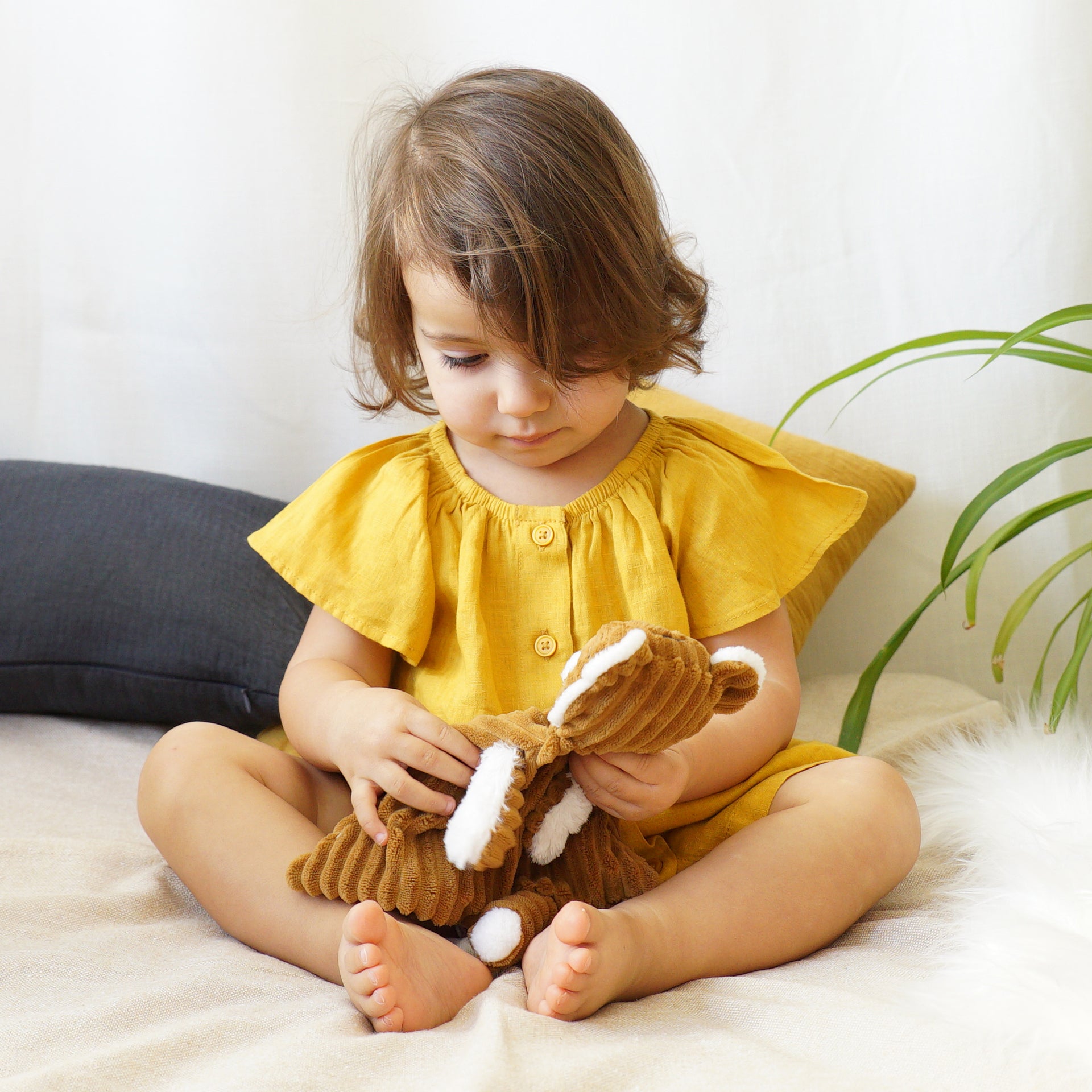 Kleinkind im gelben Kleid kuschelt braunes Plüschtier Hase – weiches Kuscheltier für Babys