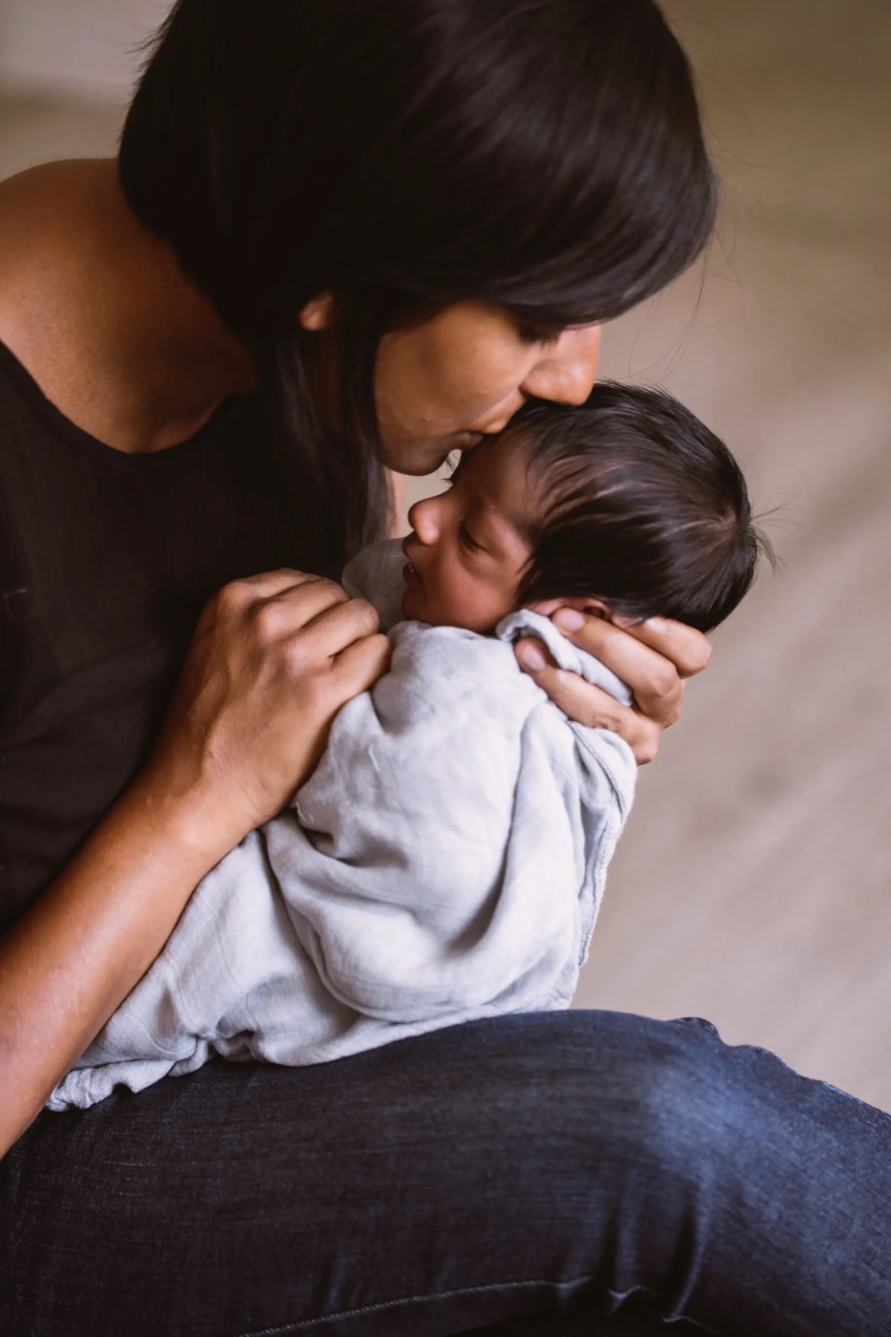 Mama hält ihr Neugeborenes im Arm und küsst es – inniger Moment voller Geborgenheit