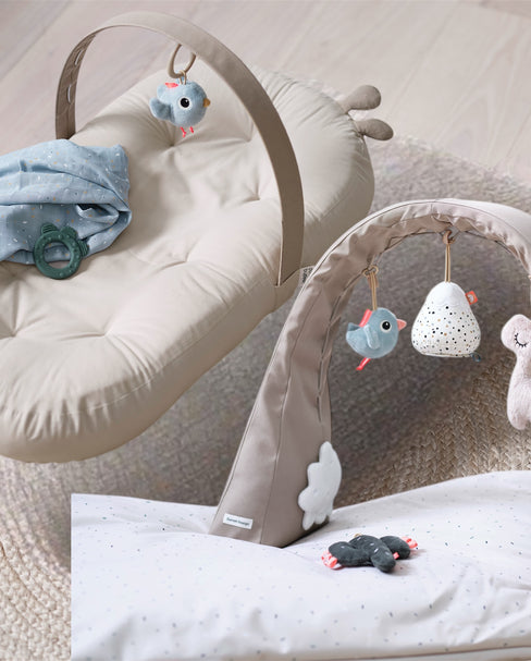 Beiges Baby Nest mit Spielbogen und Stofftieren auf natürlichem Teppich – gemütliche Spiel- und Liegefläche für Neugeborene