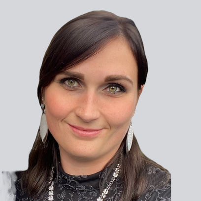 Porträtfoto der Assistentin der Geschäftsführung von BabyLions mit dunklem Haar, silbernen Ohrringen und schwarzer Bluse vor einfarbig grauem Hintergrund – professionelle Vorstellung im Teamprofil.