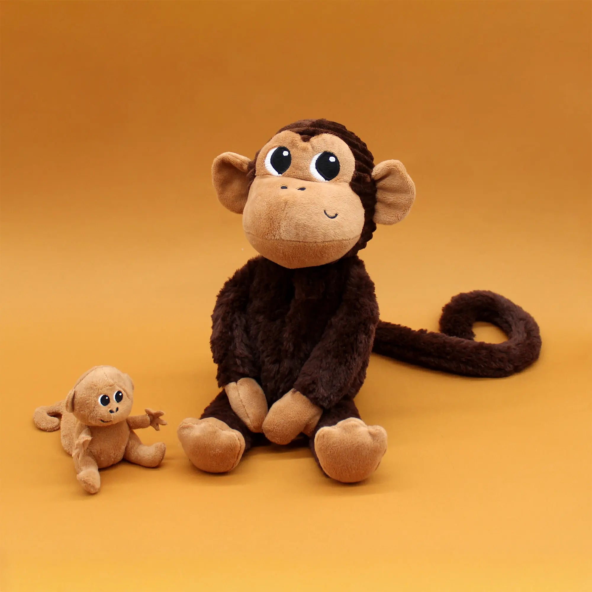 Affenmama und Baby Affe als kuschelige Plüschtiere vor orangem Hintergrund