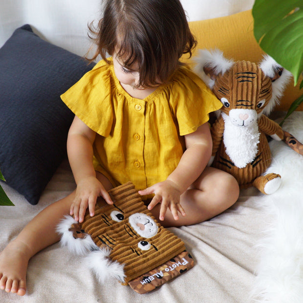 Kind sitzt auf Sofa mit Baby Fotoalbum Tiger aus Plüsch
