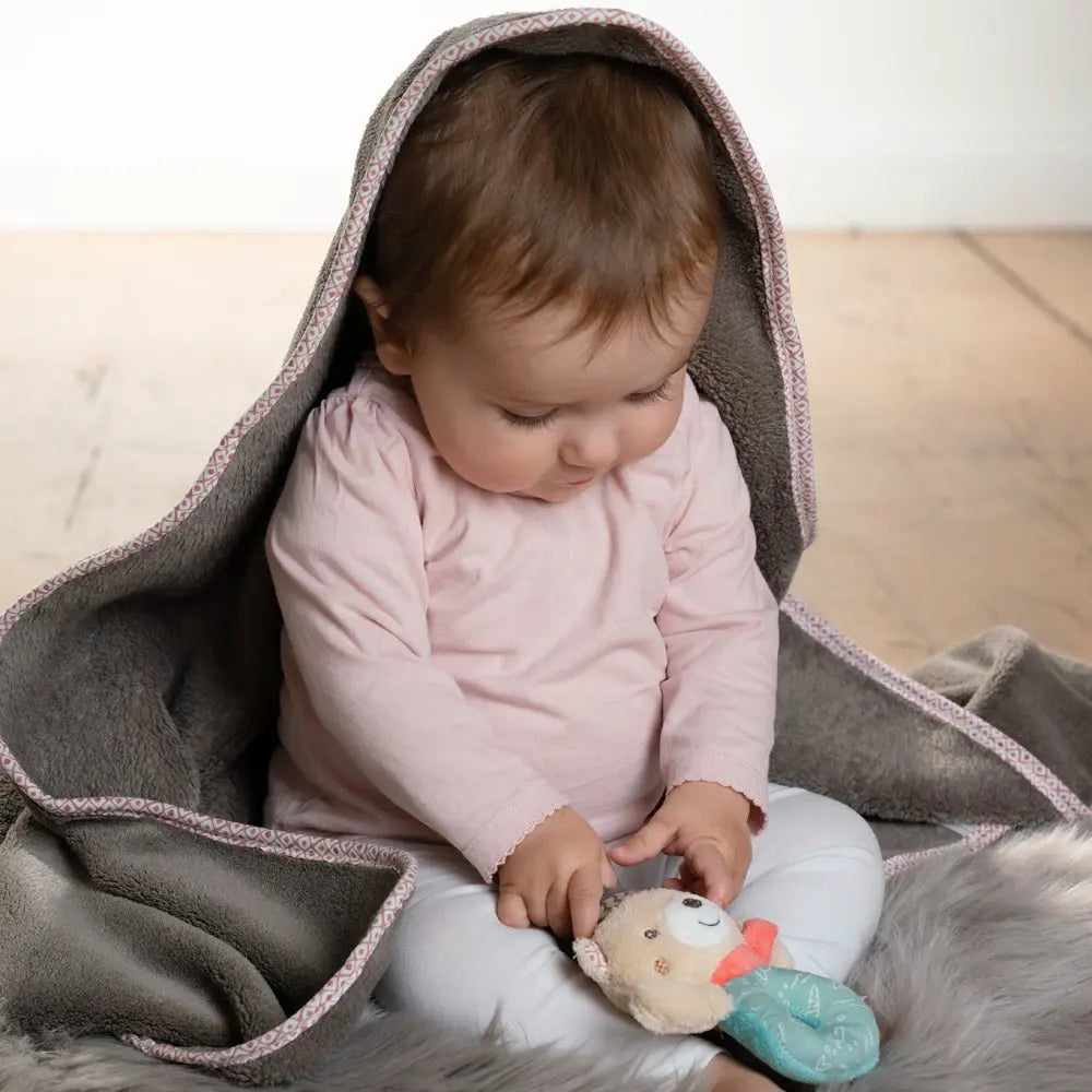 Baby Kuscheldecke Bär grau – Baby sitzt eingekuschelt unter weicher Decke und spielt mit Spielzeug