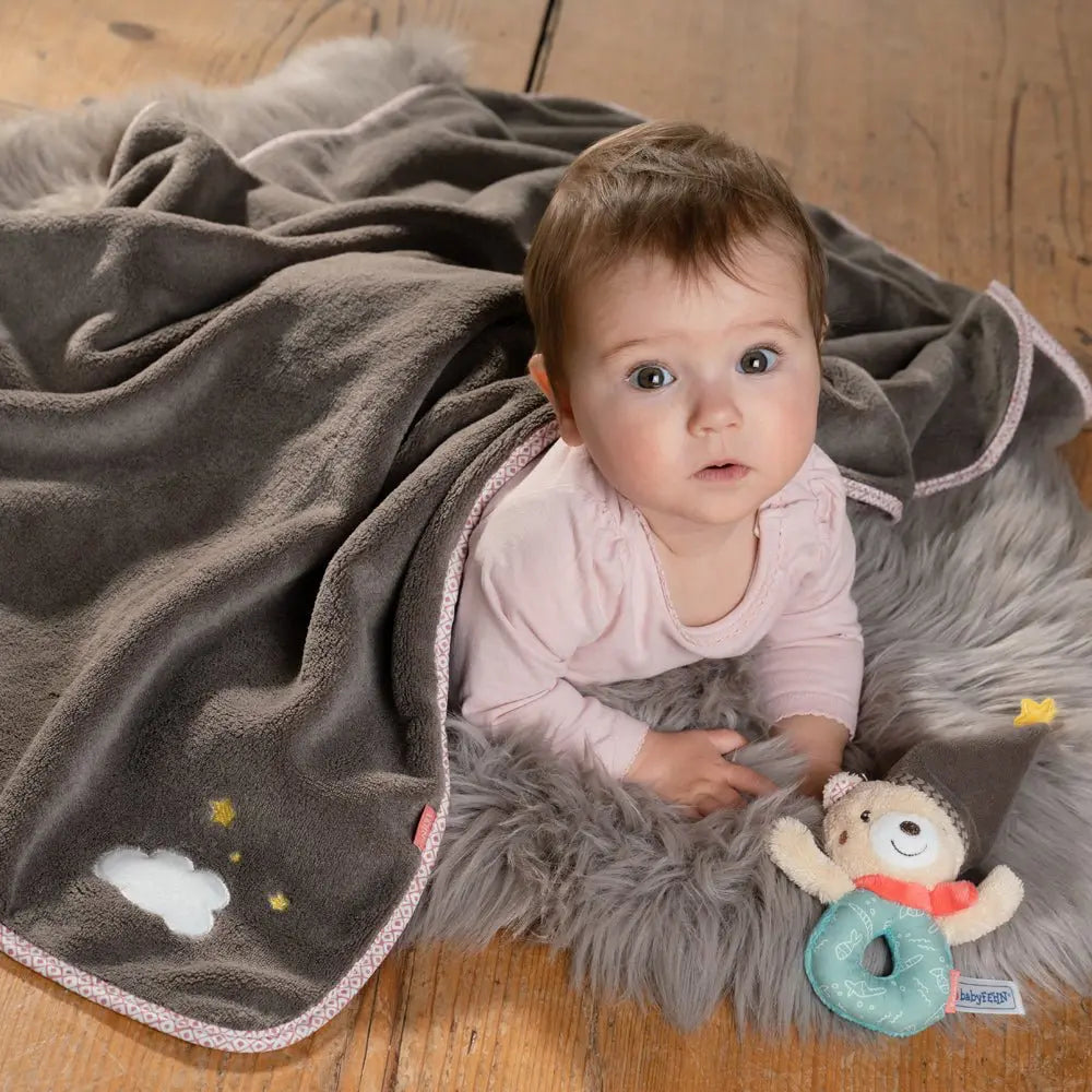 Baby Kuscheldecke Bär grau mit Sternmotiv – Baby liegt auf Decke und spielt mit Greifring Spielzeug
