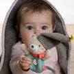Baby Kuscheldecke Bär grau mit Greifring – Baby hält Spielzeug und schaut unter der Decke hervor