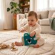 Baby sitzt auf einer Spieldecke und spielt mit einem türkisfarbenen Koala Fotoalbum für Erinnerungsfotos