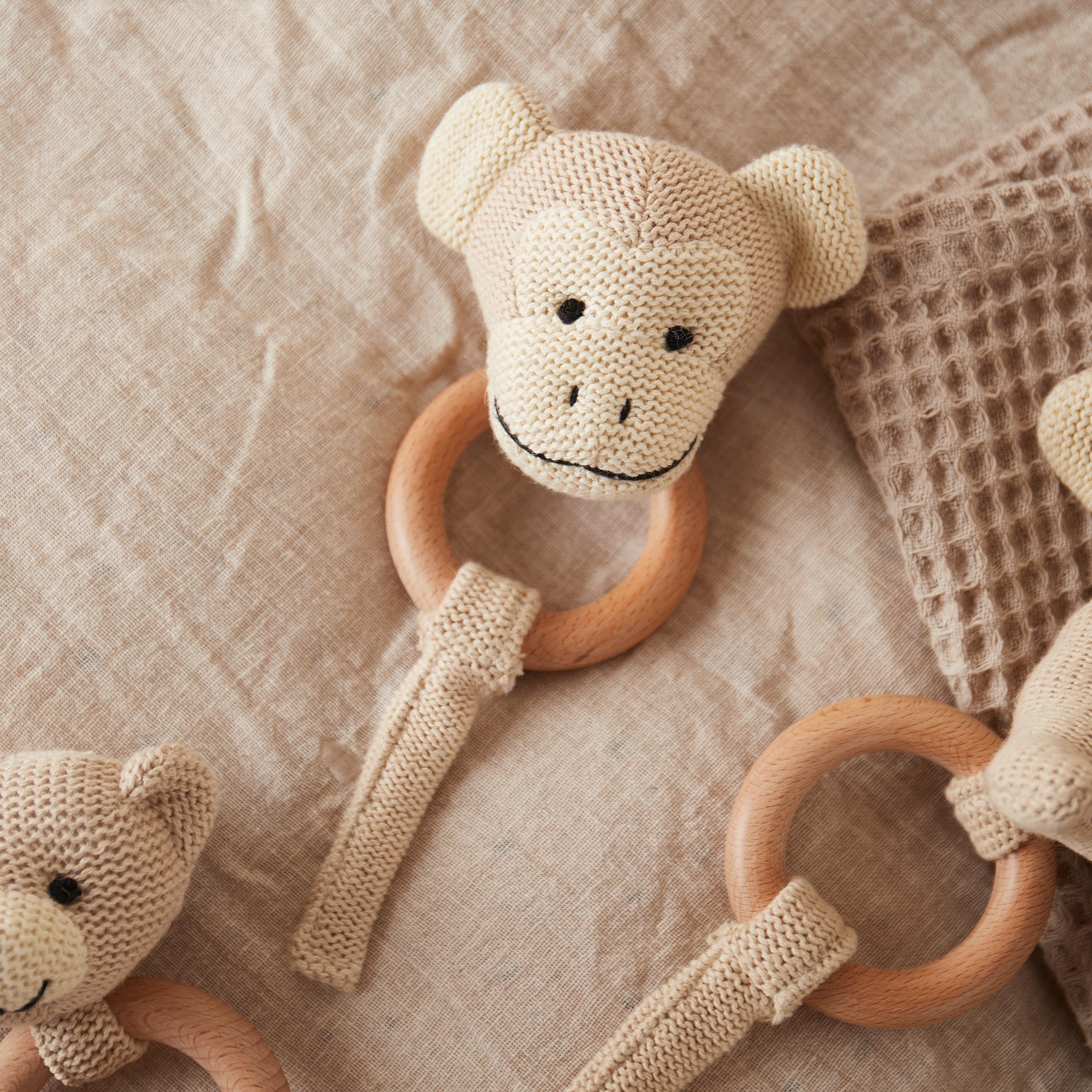Handgemachtes Greifspielzeug für Babys in Form eines gehäkelten Affenkopfs mit Holzring und Rassel von BabyLions – liegt auf beigefarbener Decke mit Waffelmuster.