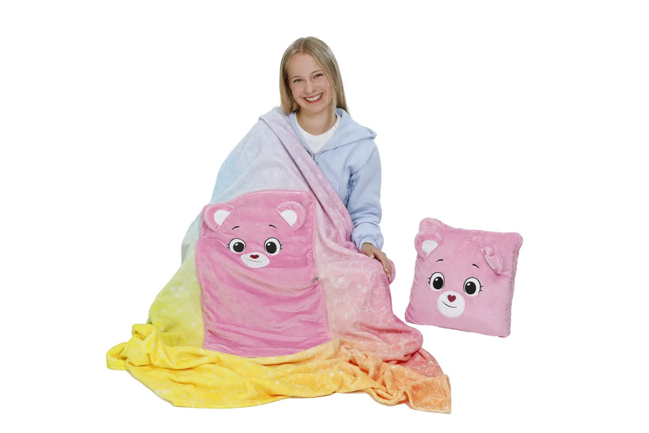 Mädchen präsentiert eine bunte Kinder-Kuscheldecke mit integriertem rosa Bärenkissen und separatem Bärenkissen.