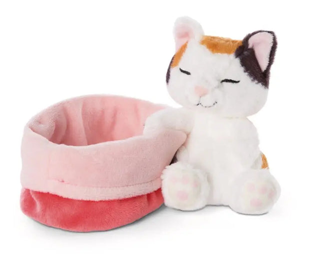 NICI Sleeping Pets Glückskatze mit dreifarbigem Fell und rosa Pfötchen, sitzend neben ihrem kuschelweichen rosa Plüschkörbchen.