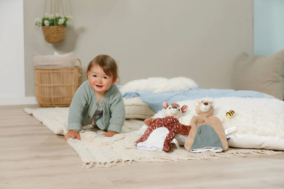 Baby spielt auf einer weichen Decke neben den NICI Handpuppen Reh und Bär aus der My First NICI Kollektion.