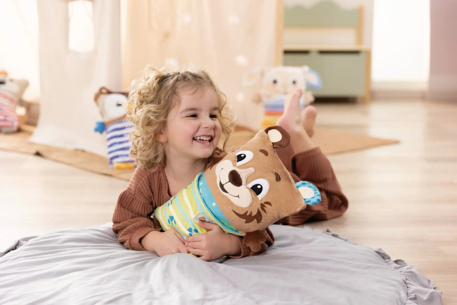 Fröhliches Kleinkind kuschelt mit dem NICI Kuscheltier Bär