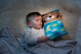 Schlafendes Kind kuschelt mit dem NICI Wendekuscheltier Bär
