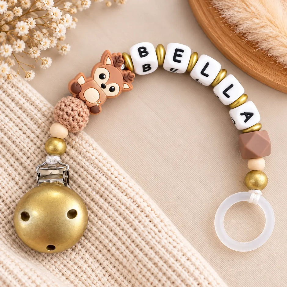 Personalisierte Schnullerkette mit Namen Bella und niedlichem Rehmotiv in Braun und Gold. Handgefertigt mit Holz-, Silikon- und Häkelperlen sowie goldenem Schnullerclip von BabyLions®.