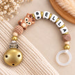 Personalisierte Schnullerkette mit Namen Bella und niedlichem Rehmotiv in Braun und Gold. Handgefertigt mit Holz-, Silikon- und Häkelperlen sowie goldenem Schnullerclip von BabyLions®.
