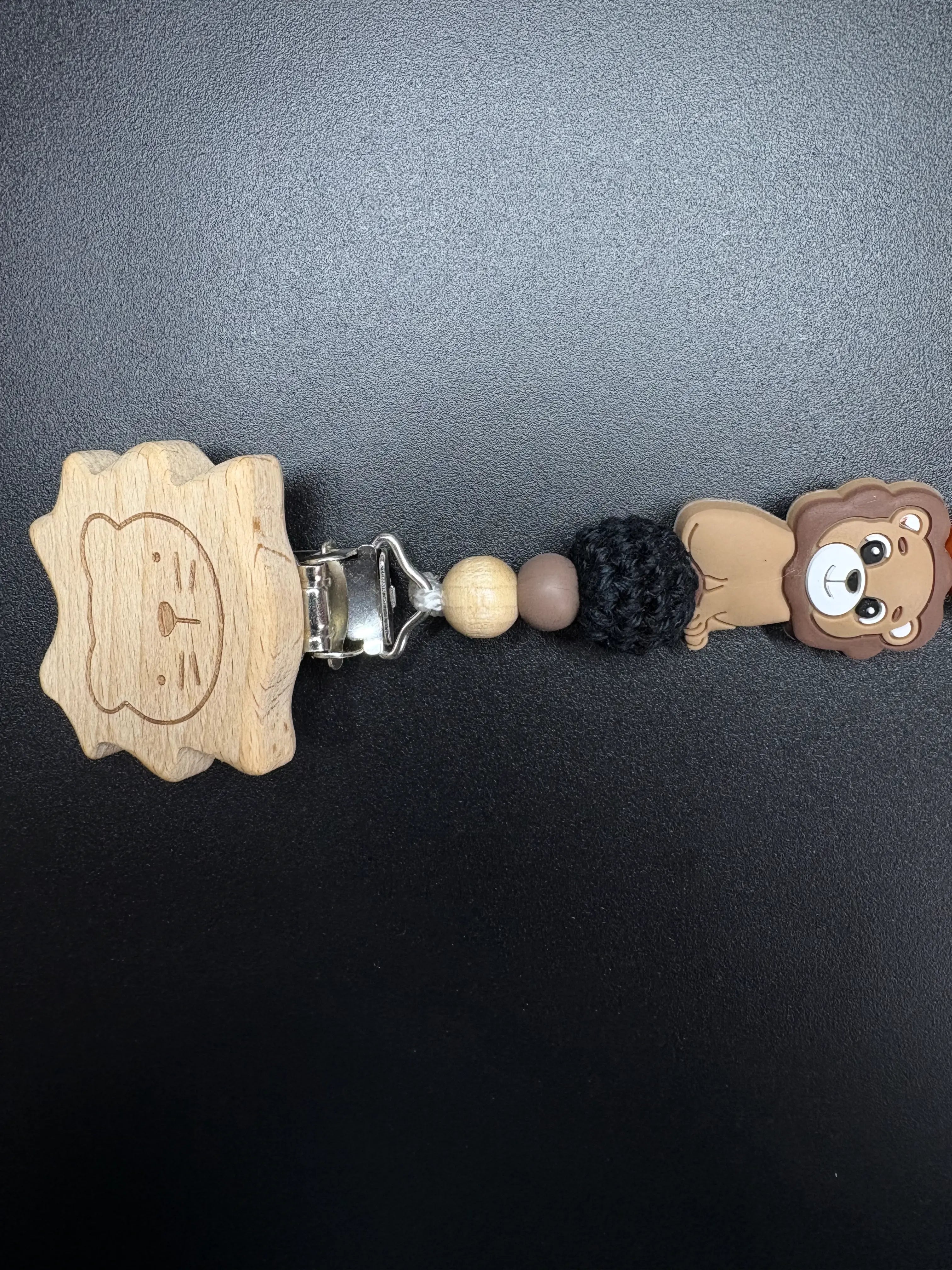 Detailaufnahme der personalisierten Schnullerkette Simba mit Holzclip, Löwenmotiv und gehäkelter schwarzer Perle