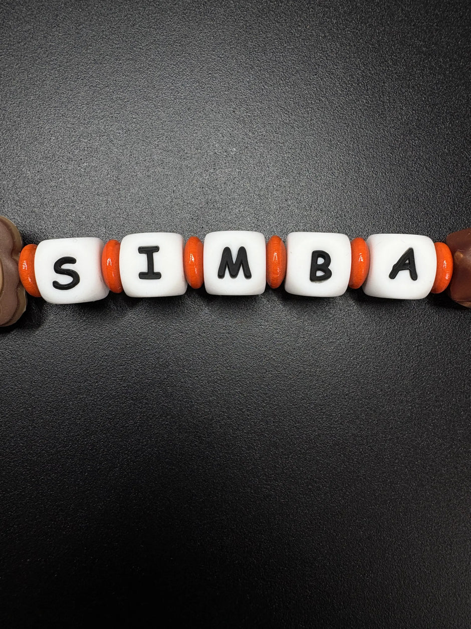 Detailaufnahme der personalisierten Schnullerkette Simba mit weißen Namensperlen und orangefarbenen Silikonringen