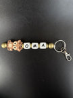 Personalisierter Schlüsselanhänger Reh von BabyLions® mit dem Schriftzug OMA, niedlichem Rehmotiv, goldfarbenen Perlen und Metallring mit Karabiner auf schwarzem Hintergrund.