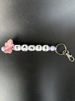 Handgefertigter personalisierter BabyLions® Schlüsselanhänger mit rosa Schmetterling, weißen Buchstabenperlen mit der Aufschrift TANTE, fliederfarbenen Perlen und silbernem Schlüsselring mit Karabiner auf schwarzem Hintergrund.