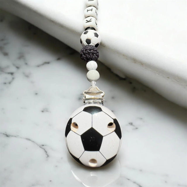 Nahaufnahme einer Schnullerkette mit Fußball-Holzclip in Schwarz Weiß