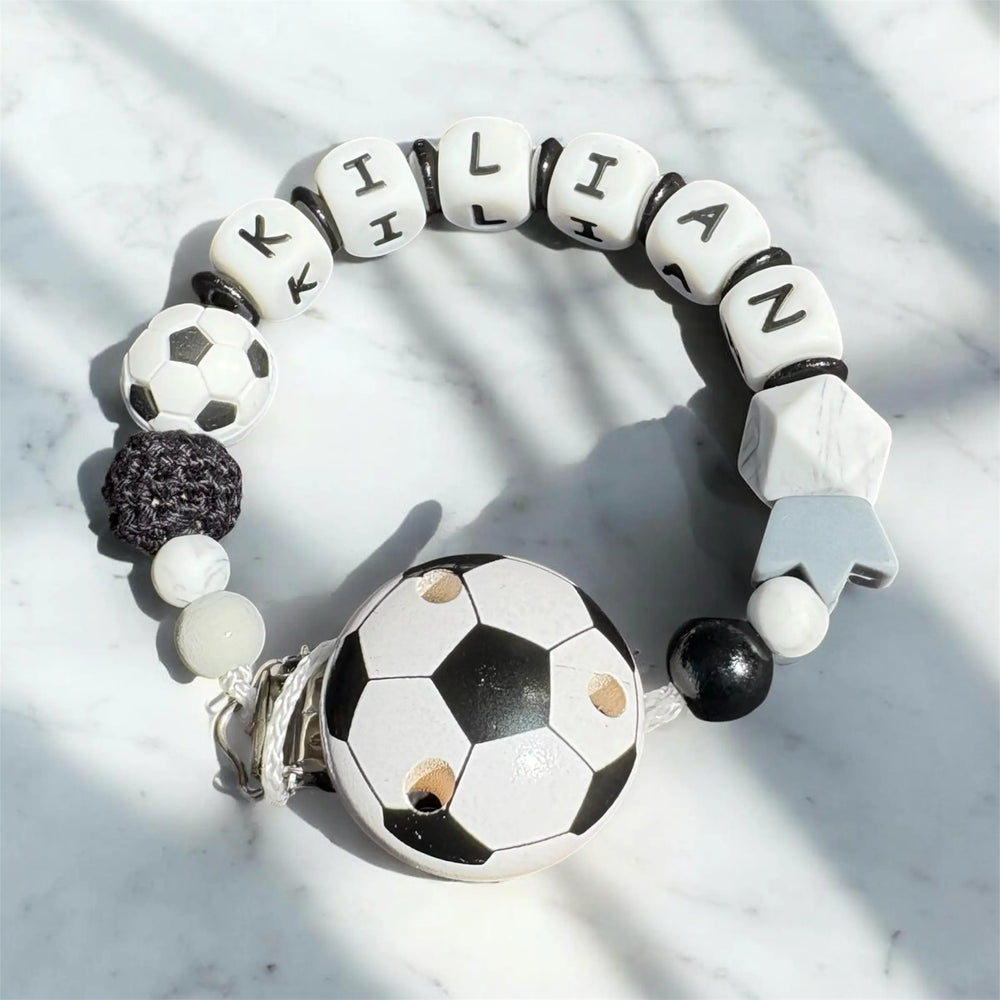 Personalisierte Schnullerkette im Fußball-Design in Schwarz Weiß mit Namen auf hellem Hintergrund